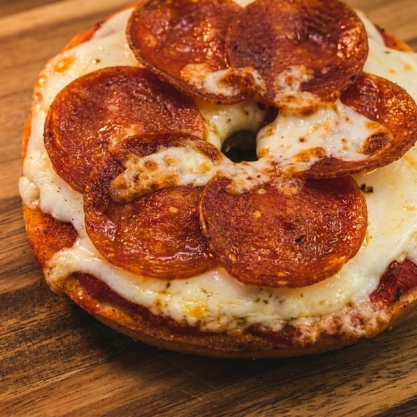 A pepperoni pizza bagel with melted cheese and tomato sauce on a wooden surface.