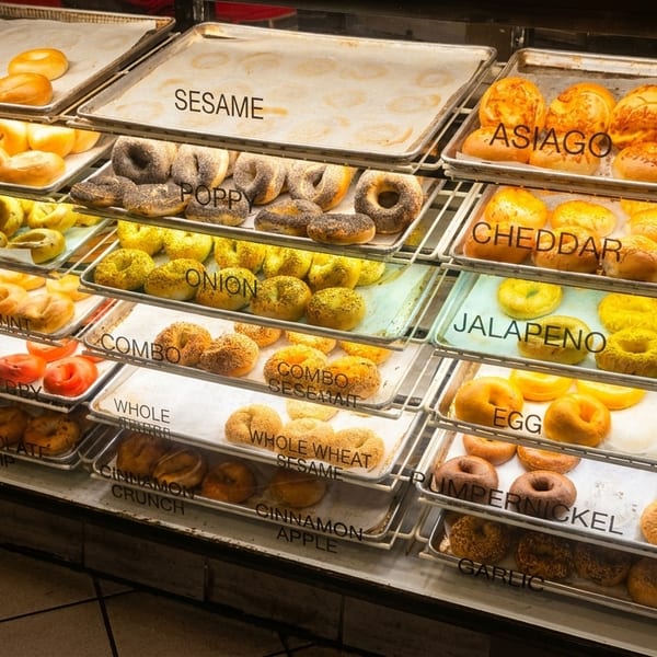 Large glass display case filled with many varieties of fresh bagels on multiple shelves.